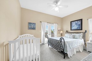 Ein Schlafzimmer mit einem Bett, einem Babybett, einem Deckenventilator und einem Fenster mit Vorhängen.