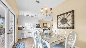 Un coin repas avec une table en verre, des chaises blanches et un lustre.