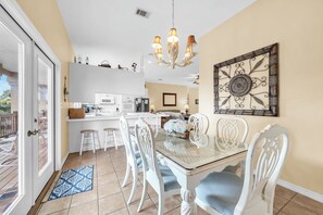 A dining area with a glass table, white chairs, and a chandelier. - Joy by the Sea large home w/ harbor views pet friendly private dock (Destin)