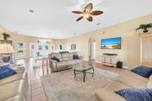 A spacious living room with a beige sofa, a glass coffee table, and a ceiling fan. - Joy by the Sea - Large Home w/ Harbor Views - Pet Friendly & Private Dock (Destin)