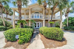 A multi-story hotel with a central entrance, surrounded by manicured landscaping and palm trees. - Joy by the Sea - Large Home w/ Harbor Views - Pet Friendly & Private Dock (Destin)