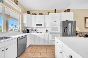 A modern kitchen with white cabinets, a stainless steel refrigerator, and a window with a view of palm trees. - Joy by the Sea large home w/ harbor views pet friendly private dock (Destin)
