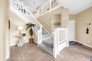 A staircase with white railings leading to an upper floor, a potted plant, a lamp, and a framed picture on the wall. - Joy by the Sea large home w/ harbor views pet friendly private dock (Destin)