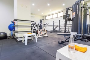 A gym with exercise equipment, a small table with a bottle, and a window. - Ocean View by Shopping Barra | Pool & A/C (Salvador)