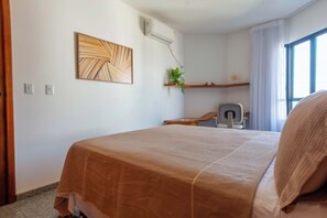 A hotel room with a bed, a desk, a chair, a plant, and a window. - Ocean View by Shopping Barra | Pool & A/C (Salvador)