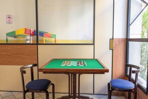 A room with a green pool table, two chairs with blue cushions, and a window with a view of greenery. - Ocean View by Shopping Barra | Pool & A/C (Salvador)