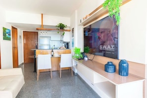 A modern kitchen with a dining area, a TV mounted on the wall, and a small plant on the counter. - Ocean View by Shopping Barra | Pool & A/C (Salvador)