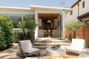 A patio with outdoor seating, a dining area, and a view into the house. - A Mesa Gem with Chic Coastal Vibes, Lush Outdoor Space, Detached Guest Studio & Hot Tub! (Santa Barbara)
