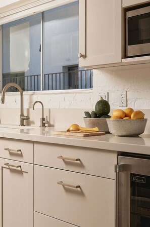A kitchen with a stainless steel sink, a microwave, and a built-in oven. There are two bowls on the counter, one with lemons and the other with a plant. - A Mesa Gem with Chic Coastal Vibes, Lush Outdoor Space, Detached Guest Studio & Hot Tub! (Santa Barbara)
