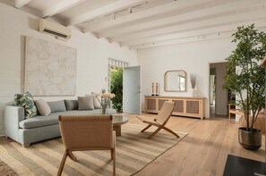 Ein geräumiges Wohnzimmer mit einem grauen Sofa, zwei Korbstühlen, einem Holzkasten und einem großen Spiegel.