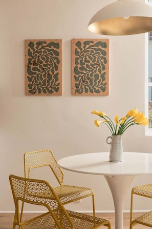 Ein Essbereich mit einem runden Tisch, zwei Stühlen mit Webmuster und zwei an der Wand befestigten Kunstwerken.