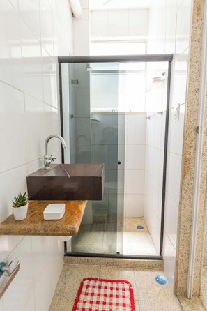 Un baño con ducha envuelta en vidrio, encimera de mármol con lavamanos y una pequeña planta en maceta.