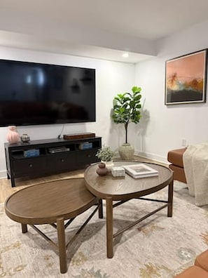 A living room with a flat-screen TV, a round wooden coffee table, a potted plant, and a painting on the wall.