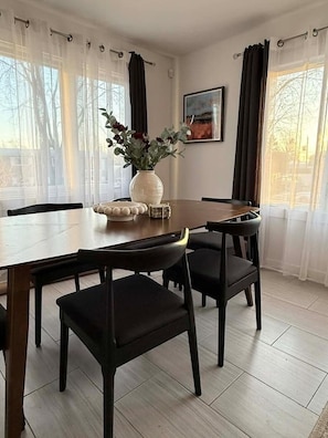 A dining area with a wooden table, black chairs, a vase with flowers, and a painting on the wall.