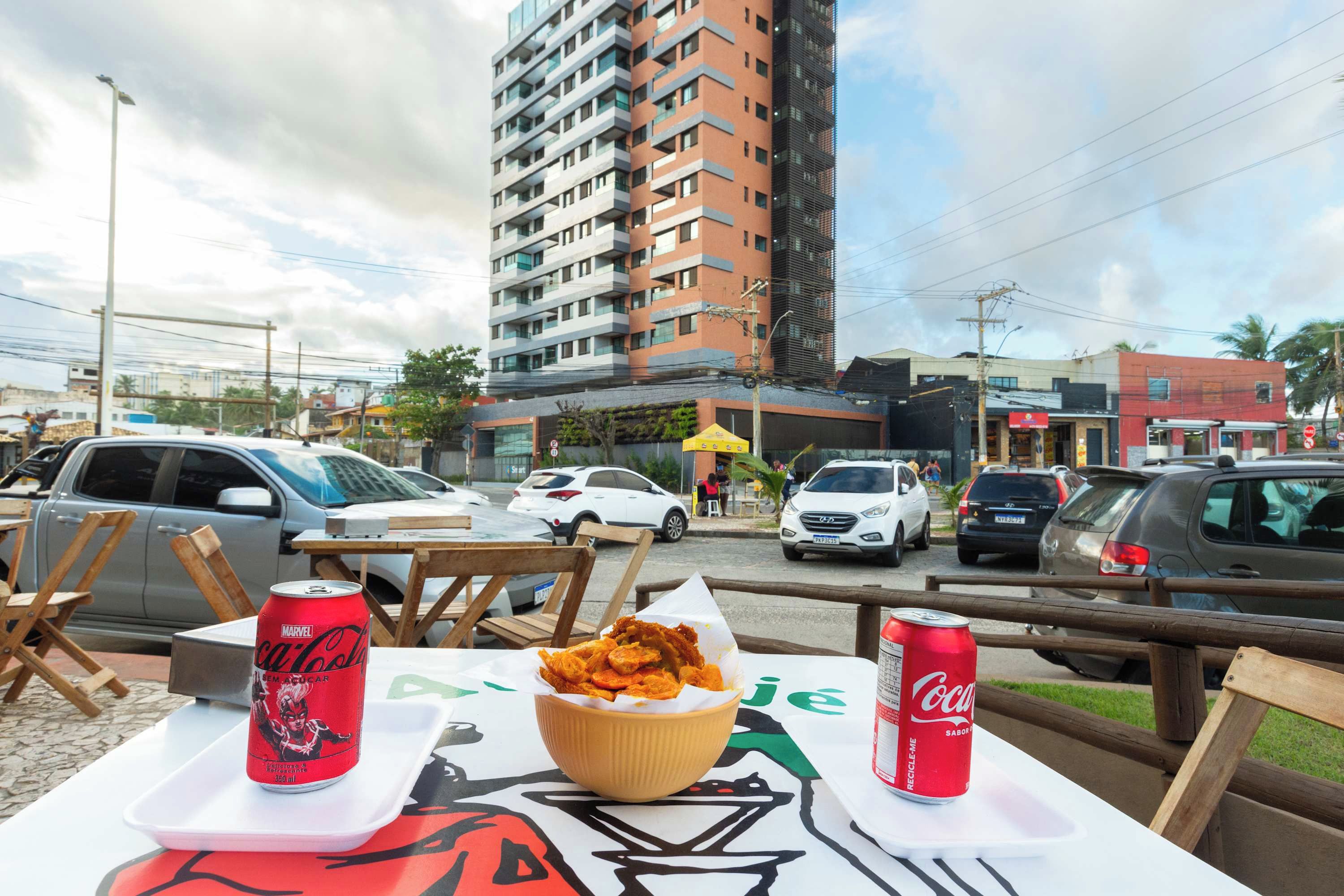 An outdoor dining area with a table set for two, featuring a bowl of fried food and two cans of Coca-Cola.