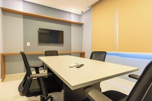 A conference room with a long table, four chairs, a flat-screen TV mounted on the wall, and a projector screen. - 2BR at Corsário Beach | Pool & A/C (Salvador)