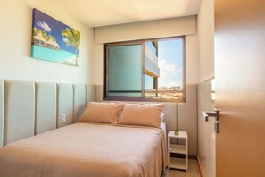 Ein Schlafzimmer mit einem Bett, einem Nachttisch, einem Fenster mit Stadtblick und einem Bild an der Wand.