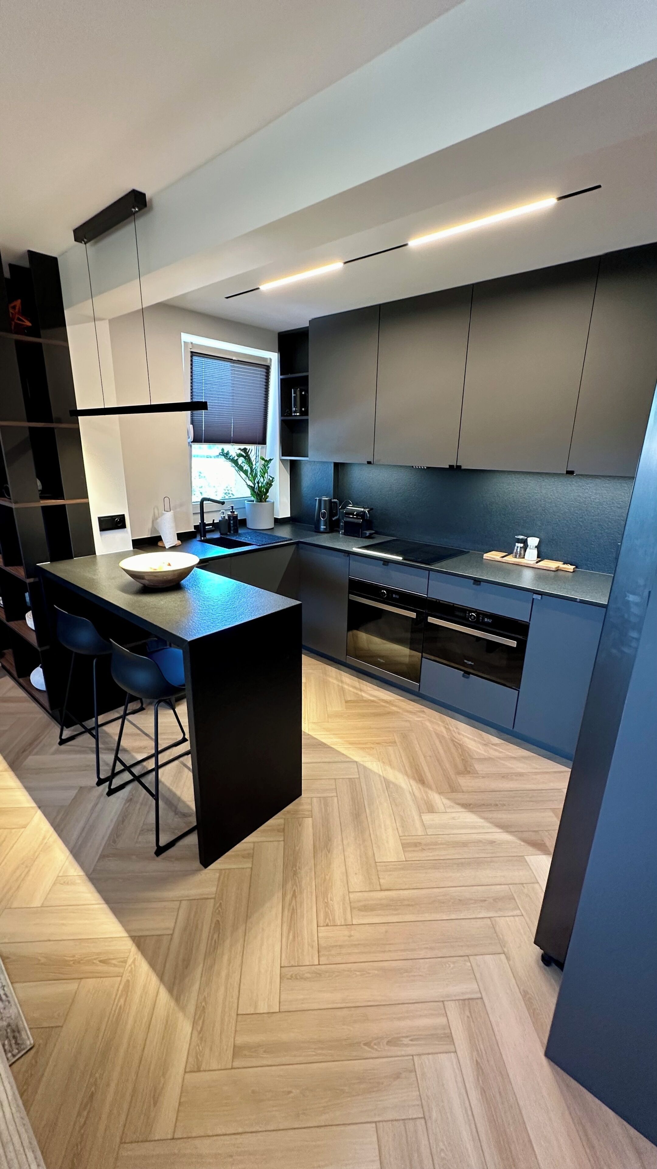 A modern kitchen with a central island, built-in appliances, and a herringbone wood floor.