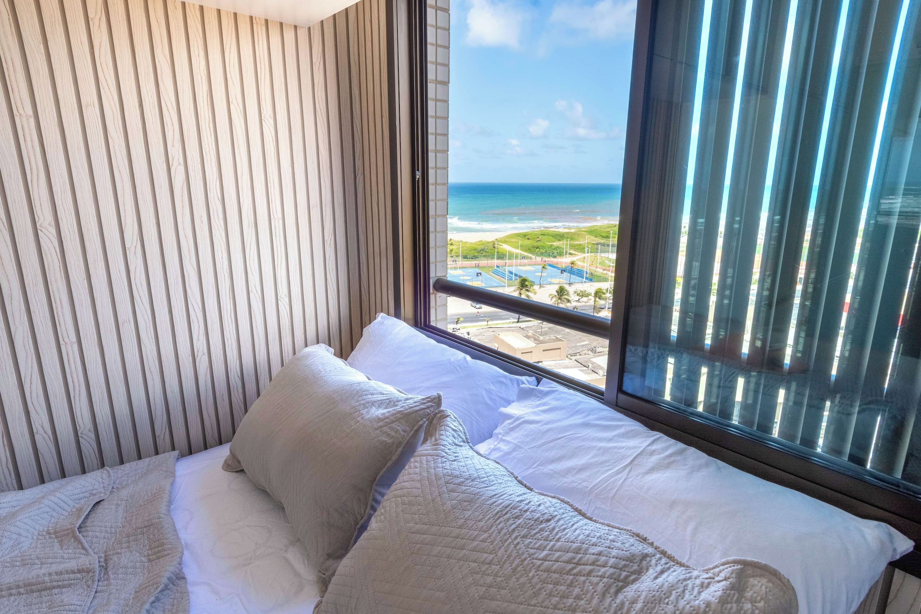 Habitación de hotel con cama, vista a la playa y ventana con persianas.