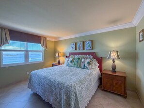 A bedroom with a bed, two bedside tables, a nightstand, a window with blinds, and a view of the sea. - Sanibel Harbour Resort -Harbour Tower 913: Enjoy the most spectacular waterfront sunsets. (Fort Myers)
