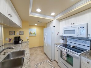 A kitchen with white cabinets, a stainless steel sink, a microwave, a refrigerator, and a stove. - Sanibel Harbour Resort -Harbour Tower 913: Enjoy the most spectacular waterfront sunsets. (Fort Myers)