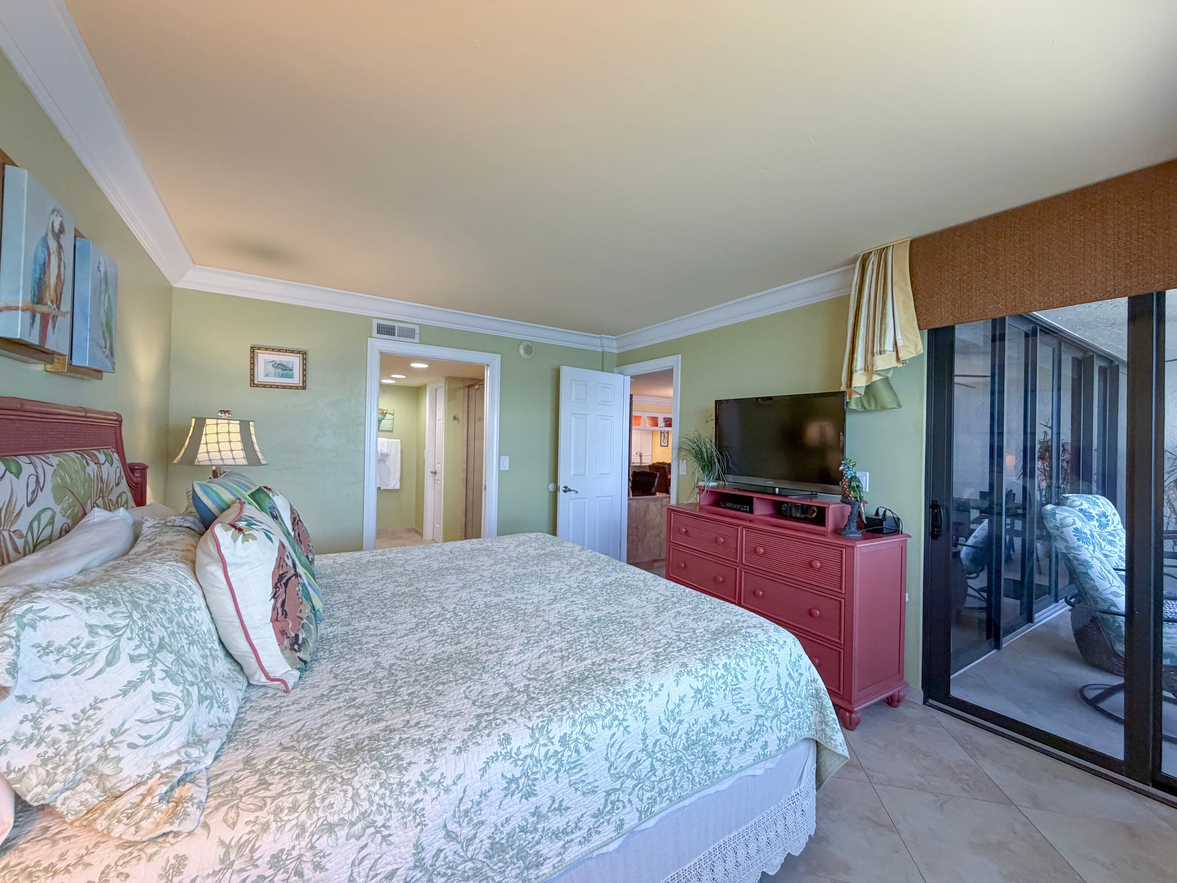 Ein Schlafzimmer mit einem Bett, einem Fernseher auf einer Kommode und einer Glastür zum Balkon.