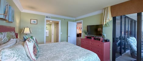 A bedroom with a bed, a television on a dresser, and a sliding glass door leading to a balcony.