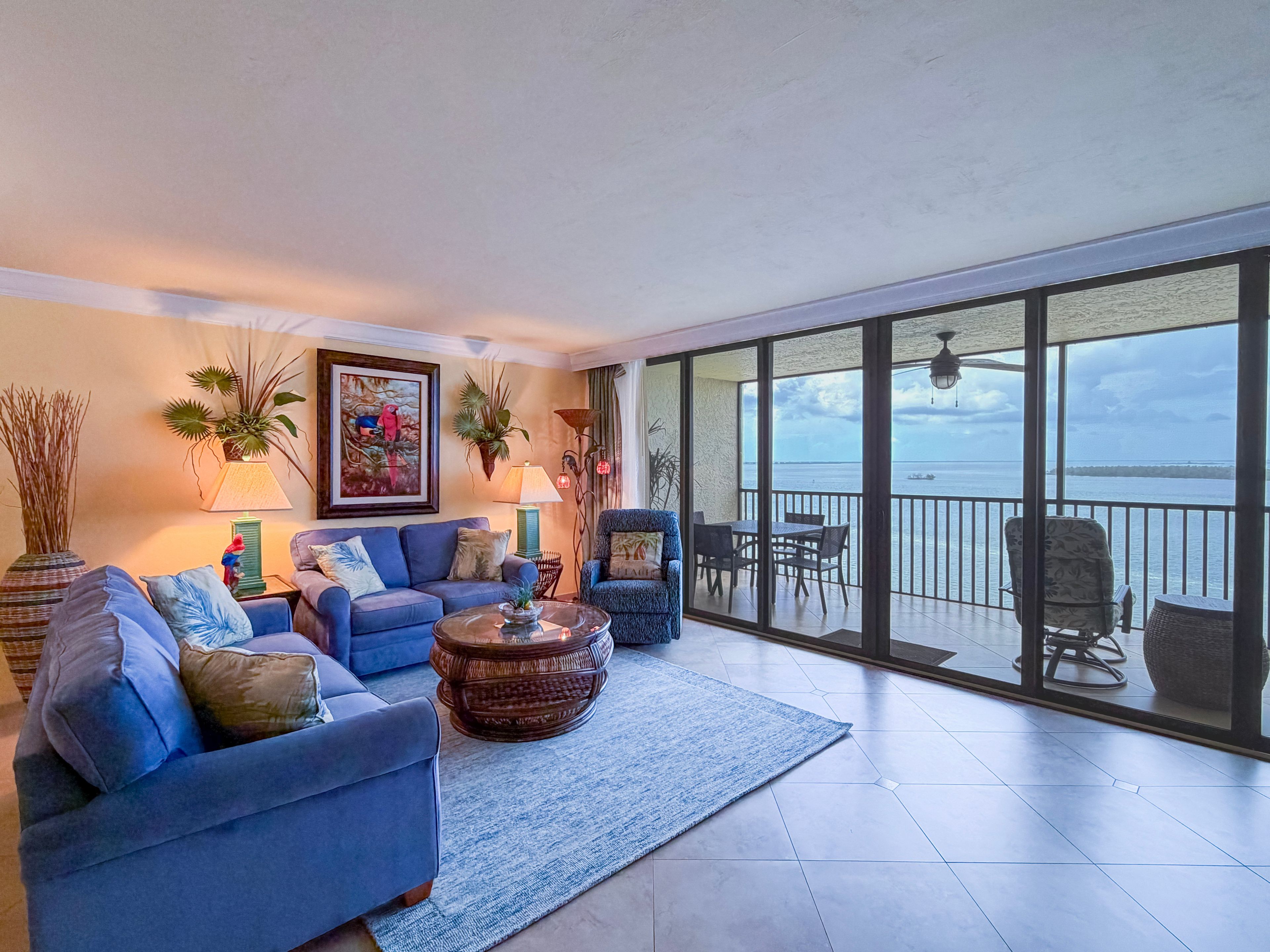 A spacious living area with a large window overlooking a body of water, furnished with a sofa, armchairs, and a coffee table.