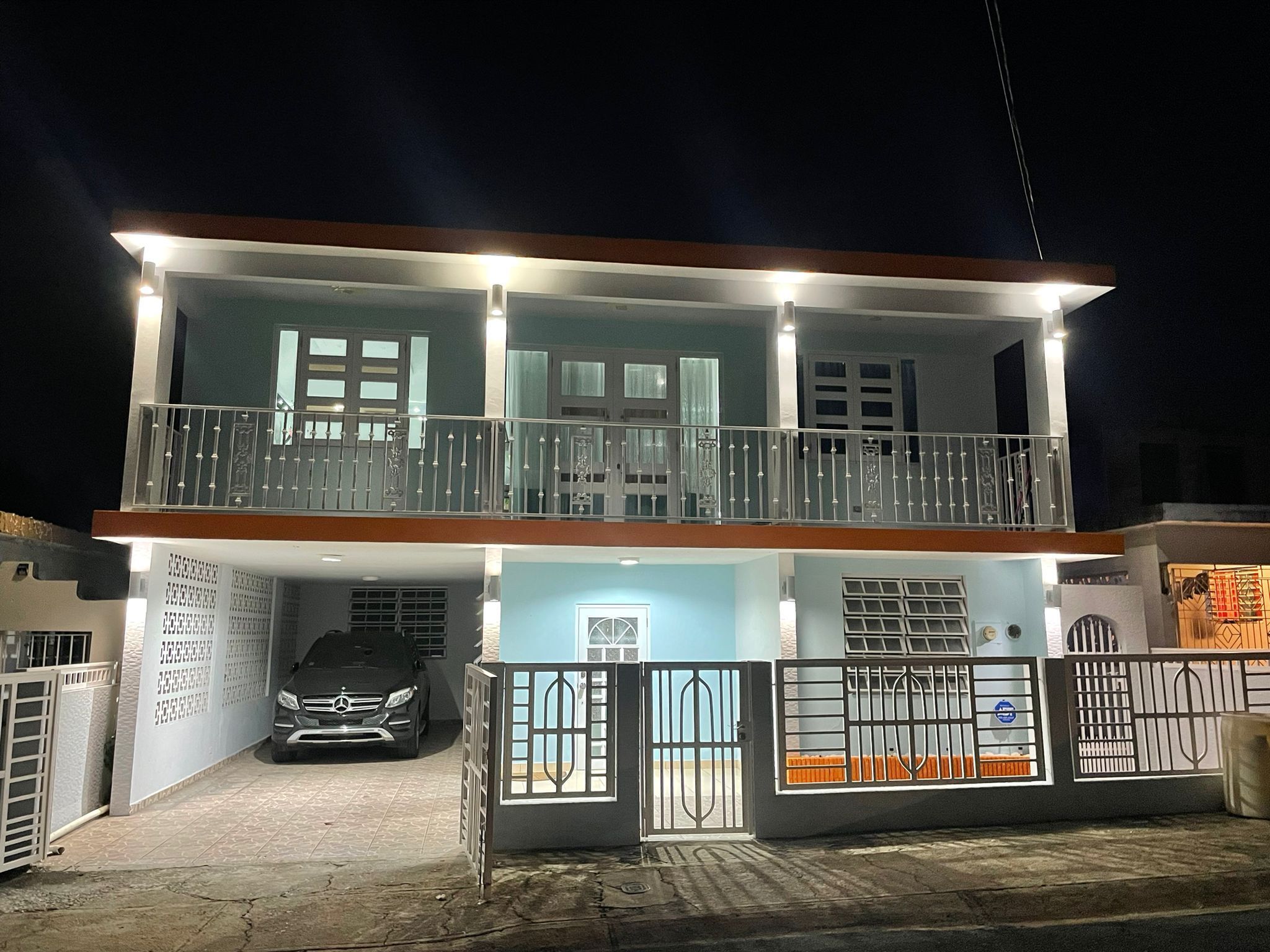 Un immeuble résidentiel à deux étages doté d’un balcon, d’un garage où se trouve une voiture et d’une entrée sécurisée par un portail.