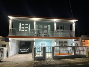 A two-story residential building with a balcony, a garage with a car, and a gated entrance. - Bright 1BR, 2-Bed Puerto Rico Apartment  10 Min to Beach  Near SJU & El Yunque (Canóvanas)