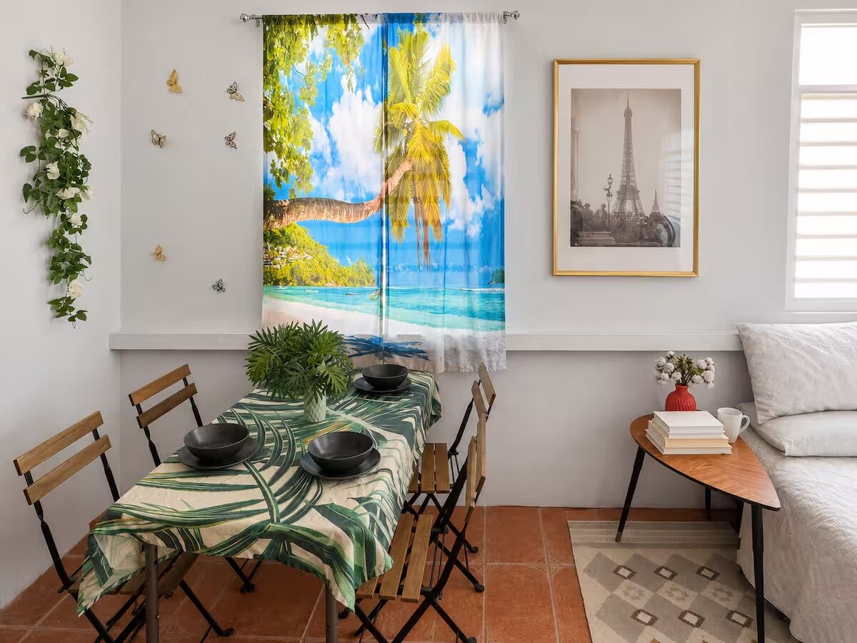 A dining area with a table set for four, a small side table with a vase and books, and a framed picture on the wall.