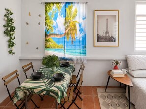 A dining area with a table set for four, a small side table with a vase and books, and a framed picture on the wall. - Bright 1BR, 2-Bed Puerto Rico Apartment  10 Min to Beach  Near SJU & El Yunque (Canóvanas)