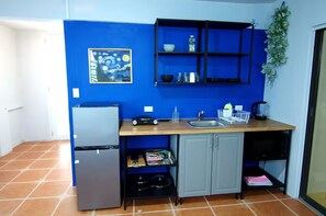 A compact kitchen with a refrigerator, a sink, and a blue wall with a painting.