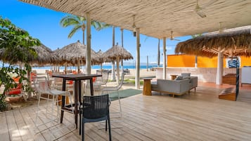 Een overdekt terras met tafels en stoelen, een bank en uitzicht op het strand en de zee.