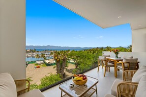 A modern living room with a large window overlooking a marina and beach. - 2BR/2BA Marina View Condo w/ King Bed, Rooftop Pool & Beach Club, La Cruz (Bahia de Banderas)