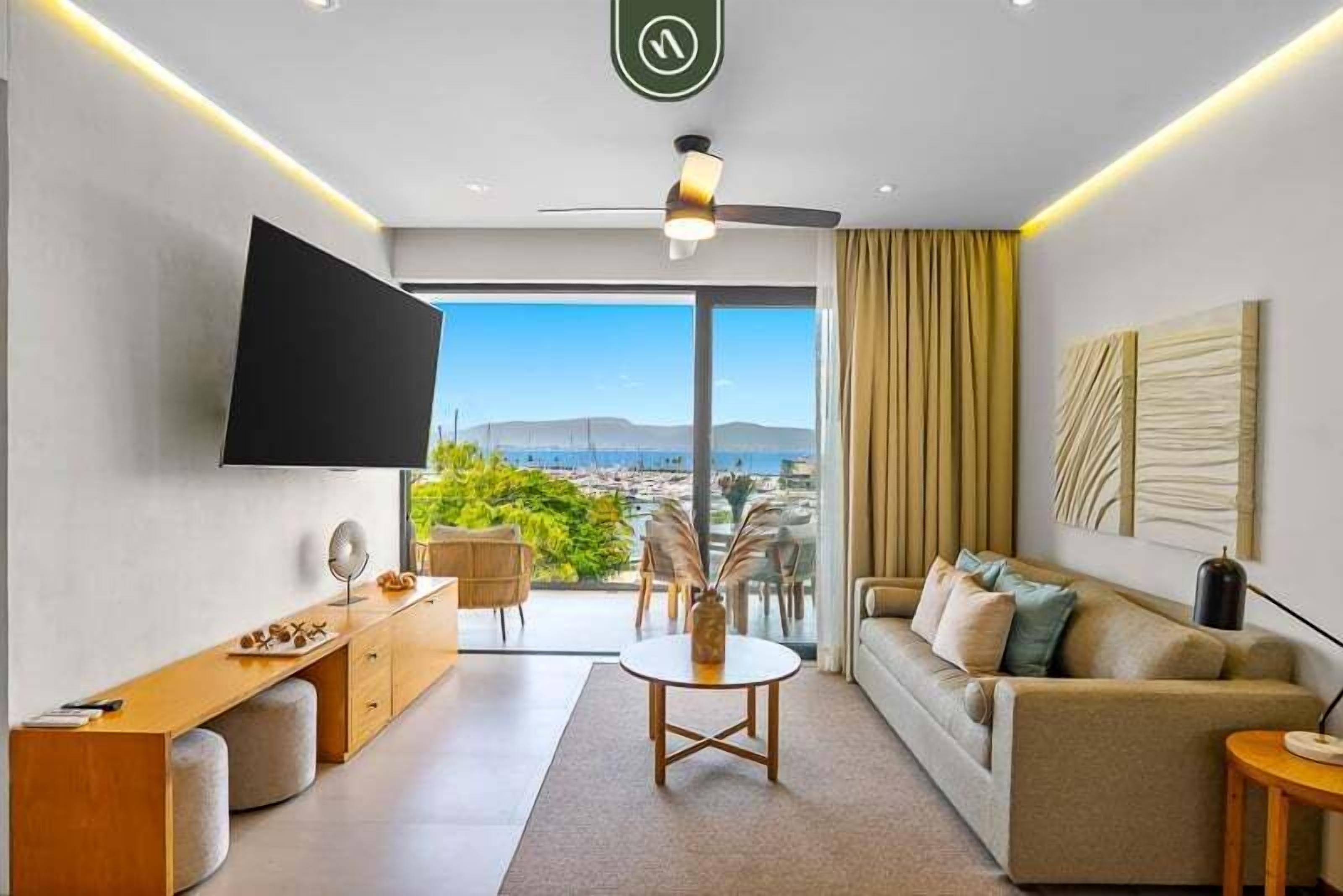 Una sala de estar moderna con televisor de pantalla plana, un sofá, una mesa de centro y vistas a la ciudad a través de amplios ventanales.