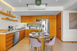 A modern kitchen with wooden cabinets, a stainless steel refrigerator, and a dining area with a round table and chairs. - 2BR/2BA Marina View Condo w/ King Bed, Rooftop Pool & Beach Club, La Cruz (Bahia de Banderas)