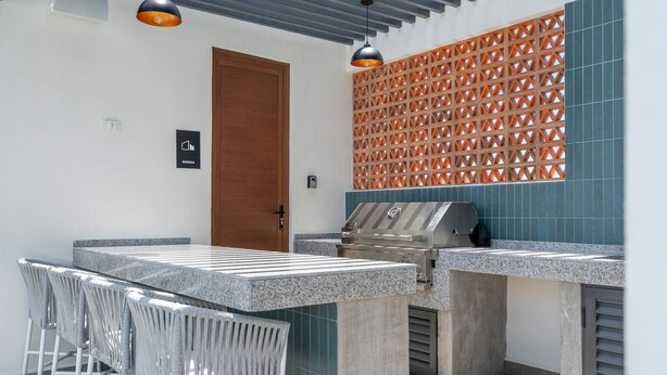 Un espace cuisine extérieur comprenant un barbecue, des tabourets de bar et des luminaires suspendus.