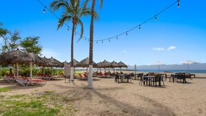 Un cadre idyllique au bord de la plage, avec des parasols en chaume, des chaises longues et des guirlandes lumineuses.