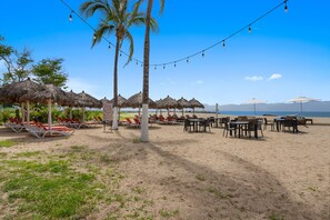 A beachside setting with thatched umbrellas, sun loungers, and string lights. - 2BR, 2BA Alik A5 condo in La Cruz with pool, gym, balcony, AC, WiFi. (Bahia de Banderas)