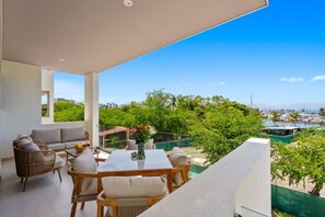 A balcony with a dining table, chairs, and a vase of flowers. - Modern 2BR Condo near Marina Riviera Nayarit | Rooftop Pool & Beach Club (Bahia de Banderas)