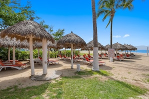 A beachside resort with thatched umbrellas, sun loungers, and palm trees. - New Listing 2BR condo near the ocean with pool, gym, WiFi, and parking. (Bahia de Banderas)