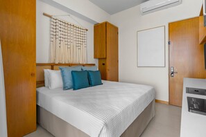 A bedroom with a bed, pillows, a wall-mounted macrame piece, wooden wardrobe, and an air conditioning unit. - Marina View Condo with Rooftop Pool & Beach Club Access – Sleeps 8 (Bahia de Banderas)