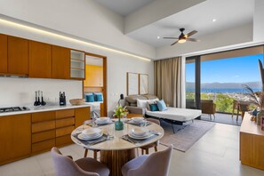 A modern kitchen with wooden cabinets, a dining area with a round table, and a view of the sea through large windows. - Marina View Condo with Rooftop Pool & Beach Club Access – Sleeps 8 (Bahia de Banderas)