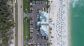 An aerial view of a hotel with a parking lot, a beach with umbrellas, and a building with a blue roof. - Awesome Private Beach Club & Pool w/ shuttle. Cozy 3-bed Condo in Bonita Bay (Bonita Springs)