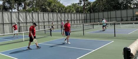 Un court de tennis avec un filet au centre, entouré d’une clôture et d’arbres.