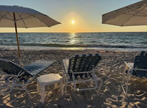 A beach with two lounge chairs and umbrellas, a small table, and the ocean in the background. - Awesome Private Beach Club & Pool w/ shuttle. Cozy 3-bed Condo in Bonita Bay (Bonita Springs)