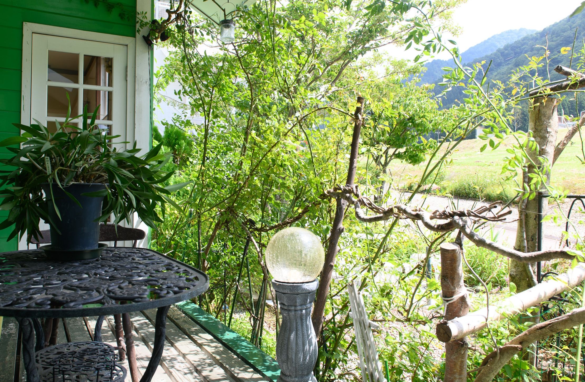 A patio with a table and chairs, surrounded by greenery and a view of the countryside.