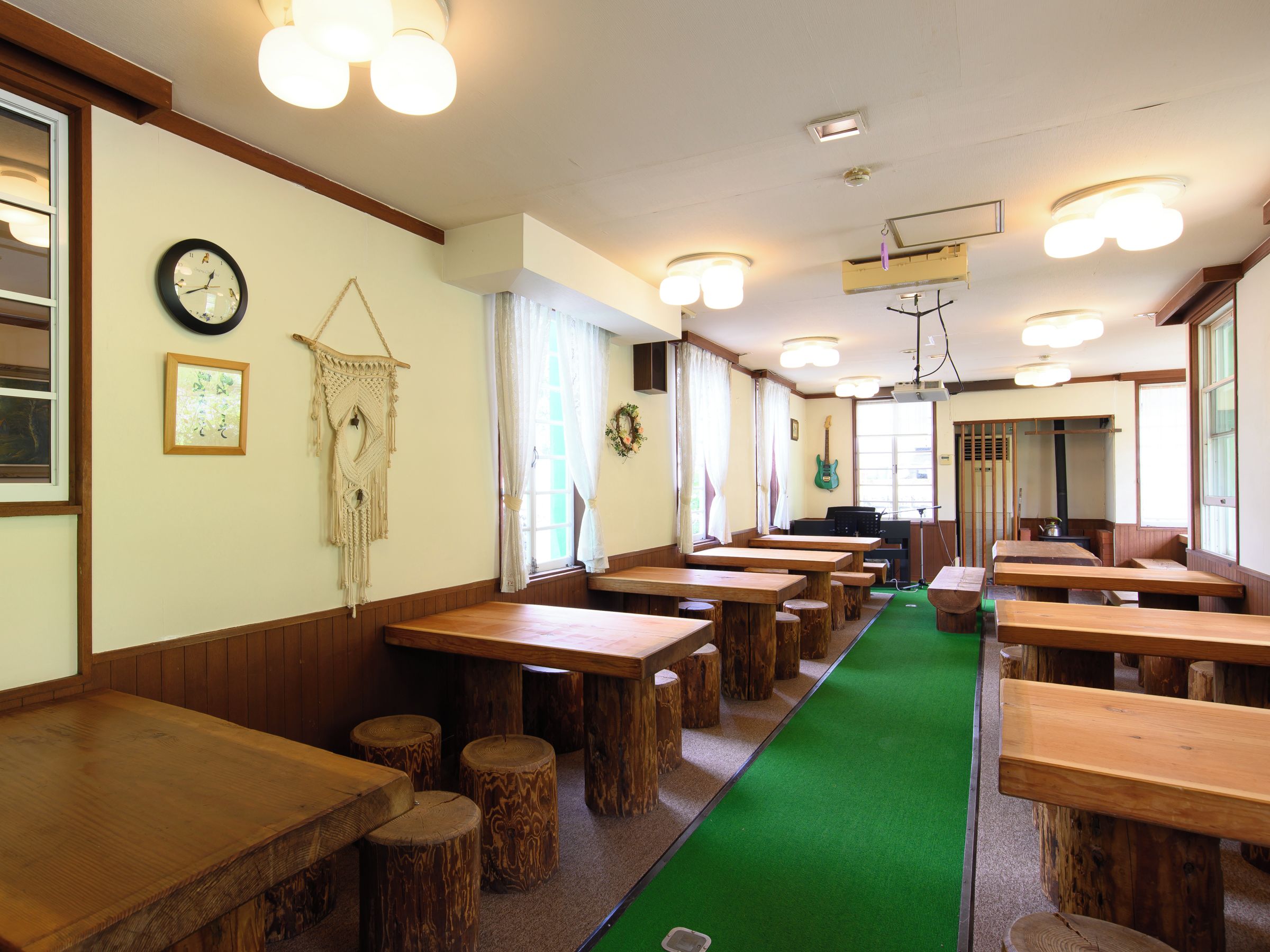 Un restaurante con mesas y bancos de madera, una alfombra verde y un reloj en la pared.