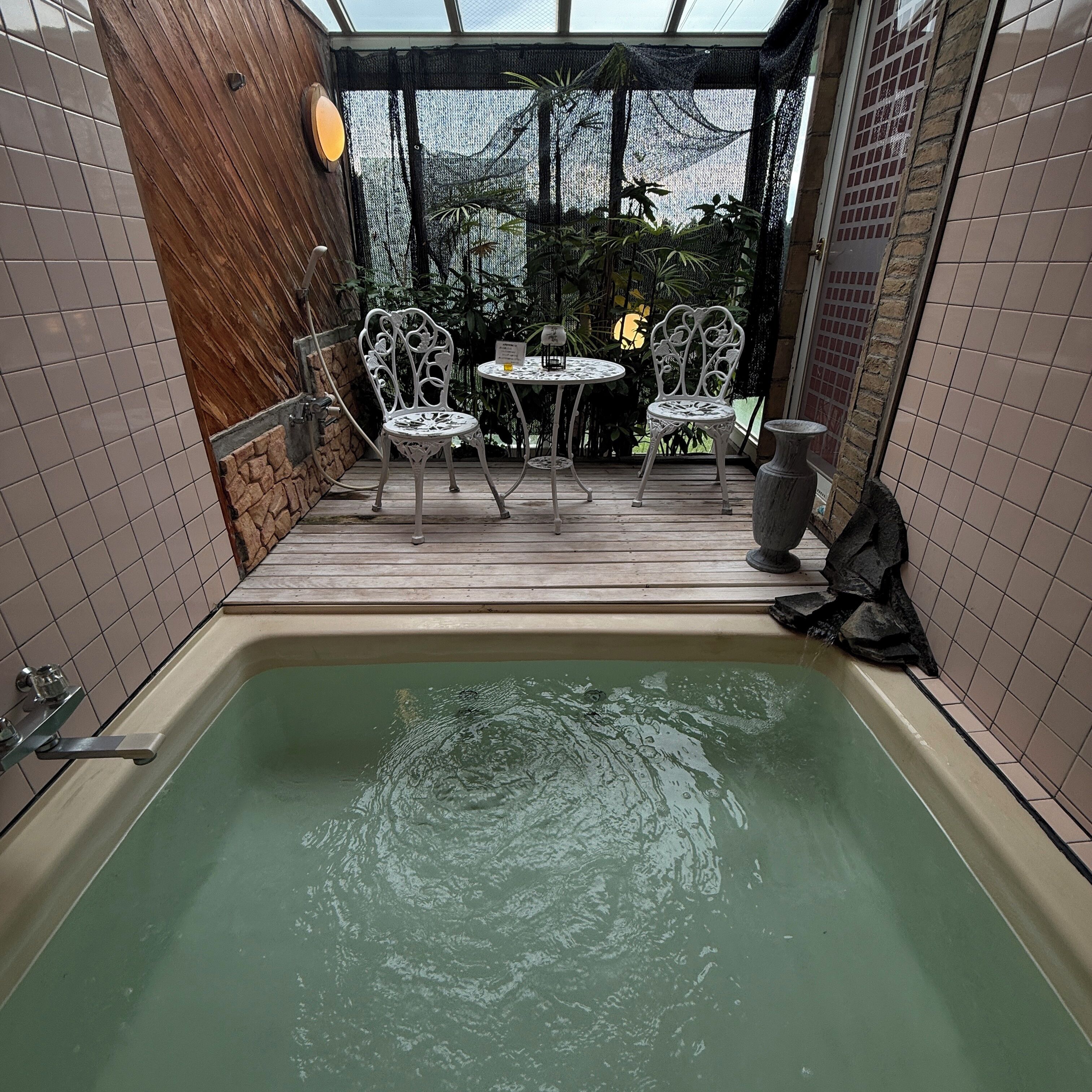 Un área de spa con un jacuzzi, dos sillas metálicas blancas y una mesa.